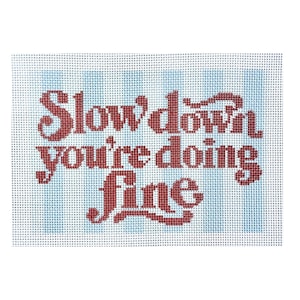 Puede incluir: Un lienzo de punto de aguja con el texto "Slow down you're doing fine" bordado en hilo rojo oscuro. El fondo consiste en rayas verticales de color azul claro sobre una malla blanca, creando un contraste claro con las letras rojas.