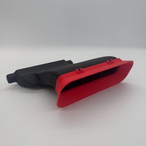 Peut inclure: Une pièce automobile noire et rouge, probablement un évent ou une prise d'air. La pièce présente un design élégant et angulaire avec une section rouge contrastante à l'avant. L'objet est en plastique ou dans un matériau similaire.