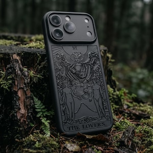 Puede incluir: Una funda de smartphone negra con un diseño grabado de la carta del tarot Los Amantes. La parte posterior de la funda muestra una figura alada central sobre dos figuras de pie, con el texto THE LOVERS y el número romano VI claramente visibles.