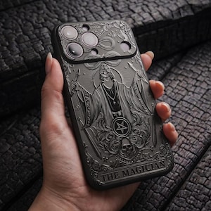 Puede incluir: Una funda de smartphone negra con un diseño en relieve de la carta del tarot El Mago. La ilustración muestra una figura con los ojos vendados que sostiene dos espadas, un símbolo de pentagrama y una calavera. El texto THE MAGICIAN aparece abajo.