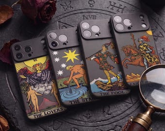 May include: Four black smartphone cases featuring tarot card illustrations. The designs include The Lovers, The Star, The Fool, and Knight of Wands. Each case has a camera cutout and is arranged on a dark circular stone surface with a magnifying glass.