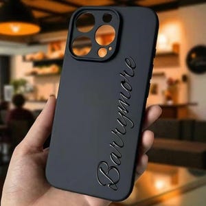 May include: A matte black phone case with cutouts for the camera and buttons. The name "Barrymore" is embossed in a cursive font on the back of the case. The case is designed to protect a smartphone.