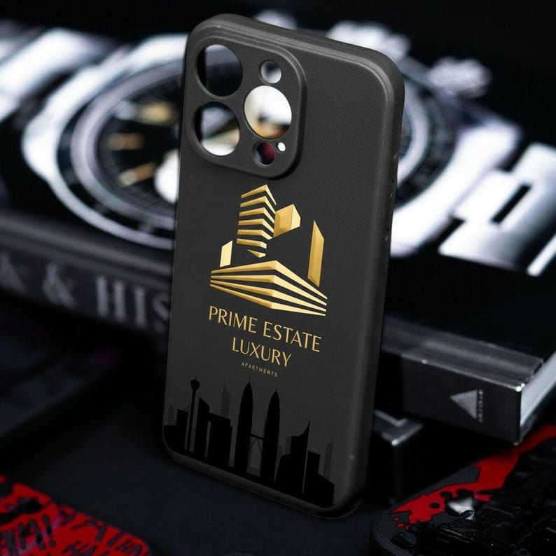 Pu&ograve; includere: Custodia per telefono nera con un logo dorato raffigurante un design di edificio e la scritta "PRIME ESTATE LUXURY APARTMENTS". Una silhouette di skyline &egrave; in basso. La custodia ha ritagli per la fotocamera e i pulsanti del telefono.