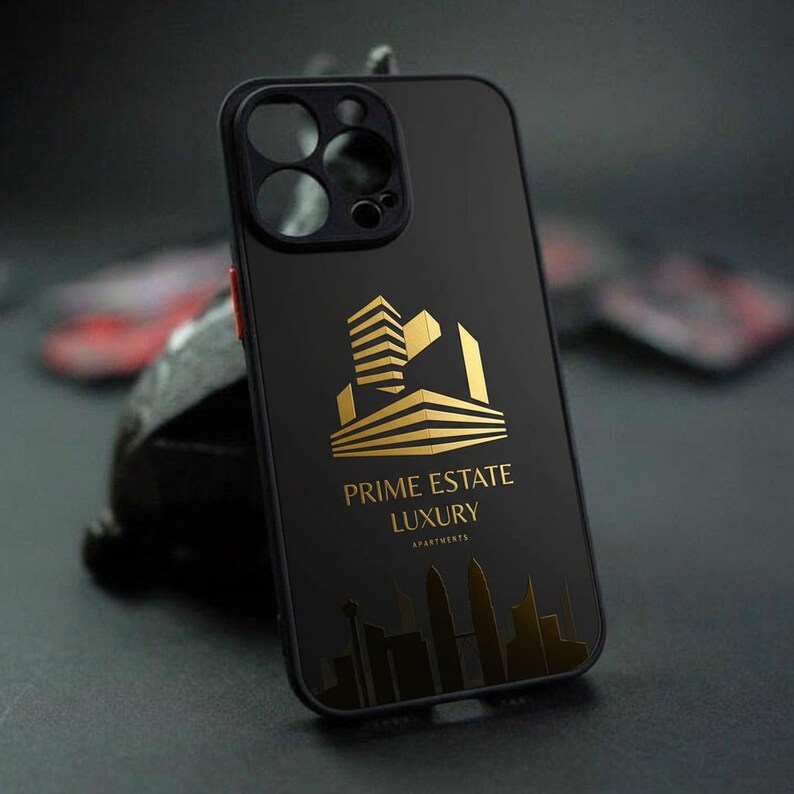 Pu&ograve; includere: Custodia per telefono nera con logo dorato "Prime Estate Luxury Apartments". Il logo presenta un design stilizzato di un edificio. La custodia ha un design elegante e moderno.