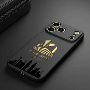 Pu&ograve; includere: Custodia per telefono nera con dettagli dorati e la scritta "PRIME ESTATE LUXURY". La custodia presenta un logo dorato e una silhouette di paesaggio urbano. La custodia del telefono ha un rilievo della fotocamera con tre lenti.