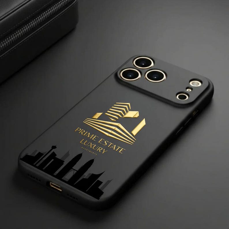 Pu&ograve; includere: Custodia per telefono nera con dettagli dorati e la scritta "PRIME ESTATE LUXURY". La custodia presenta un logo dorato e una silhouette di paesaggio urbano. La custodia del telefono ha un rilievo della fotocamera con tre lenti.