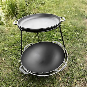 Puede incluir: Una sartén de hierro fundido negra con mango se encuentra sobre un soporte de metal negro con tres patas. Una segunda sartén de hierro fundido negra con mango está encima del soporte.
