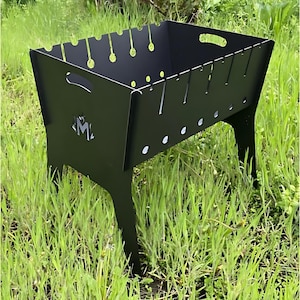 Könnte beinhalten: Schwarzer Feuerkorb aus Metall mit rechteckiger Form und vier Beinen. Der Feuerkorb hat ein ausgeschnittenes Design an den Seiten und ein Logo mit der Aufschrift "JM2" auf der Vorderseite.