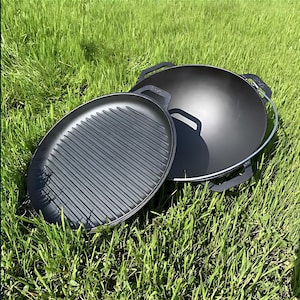 Op de afbeelding: Twee zwarte gietijzeren kookgerei-onderdelen, een ronde grillpan en een wok met een handvat, op een groene grasmat.