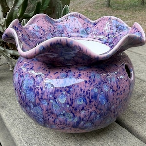 May include: A ceramic oil warmer with a ruffled rim, in shades of purple and blue. The speckled design covers the round base and the wavy top. A hole is visible on the side of the base.
