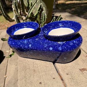 May include: A white ceramic mug with a black handle and the text "But First, Coffee" in a bold, black font. The mug is set against a blurred background, suggesting a cozy setting.