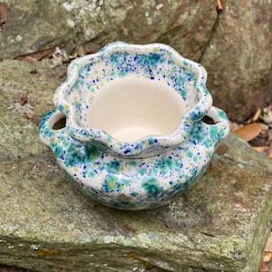 May include: A two-piece ceramic bowl set with a scalloped rim. The bowls are white inside and have a speckled pattern of blue, green, and yellow on the outside. The bowls have small handles.