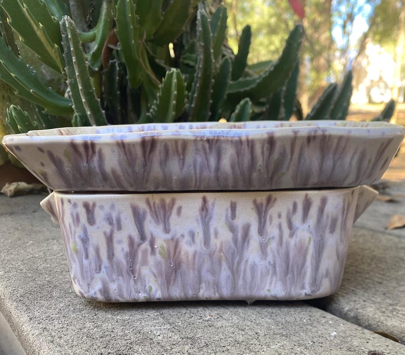 May include: Two ceramic rectangular planters stacked. The planters have a speckled glaze in lavender, brown, and cream. The top planter has a different shape. The planters are on a concrete surface. The planters are suitable for small plants or succulents.