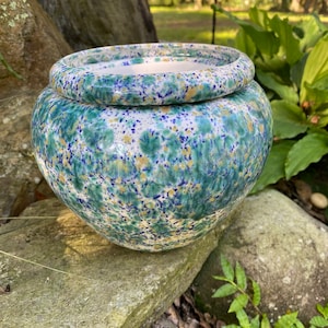 May include: A ceramic planter with a speckled design in shades of blue, green, and yellow. The round pot has a matching rim and sits on a stone surface. The planter is suitable for indoor or outdoor use.