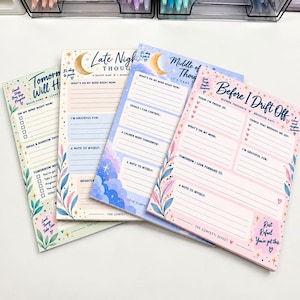 May include: Four rectangular paper notepads with pastel color schemes and celestial motifs. Each pad features printed prompts for daily reflection, including sections like "Late Night Thoughts," "Middle of the Night," and "Before I Drift Off."