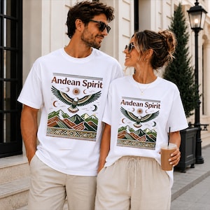 Puede incluir: Dos camisetas blancas con un estampado gráfico que incluye el texto Andean Spirit, un águila volando, un sol, lunas y picos montañosos estilizados en tonos verde, marrón y naranja, con un borde geométrico en la parte inferior del diseño.