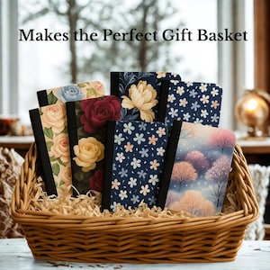 Könnte beinhalten: Ein Weidenkorb gefüllt mit Notizbüchern mit floralen und naturbezogenen Designs. Die Notizbücher haben schwarze Rücken und verschiedene Einbände mit Rosen, Pfingstrosen und anderen Blumenmustern. Der Text "Makes the Perfect Gift Basket" steht oben.