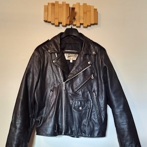 Könnte beinhalten: Schwarze Leder-Motorradjacke mit silbernem Reißverschluss und mehreren Taschen. Die Jacke hängt an einem schwarzen Kleiderbügel. Das Etikett lautet "OPEN ROAD".
