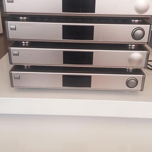 以下が含まれることがあります： 4つの銀色のオーディオコンポーネントが積み重ねられています。 上部のコンポーネントには、前面に「Panasonic」という文字があります。