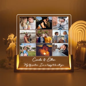 May include: A personalized LED photo frame with a collage of nine photos of a couple. The frame has a wooden base and a clear acrylic panel. The text "Camila & Ethan" and "My life partner. I am so happy to be with you." is displayed on the frame.