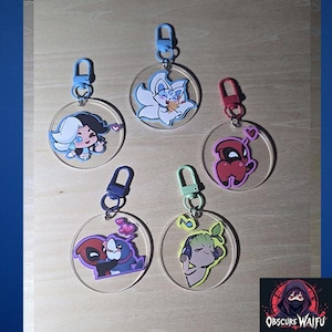 May include: A collection of five clear acrylic keychains with colorful cartoon character designs. Each keychain has a different character, including a white-haired figure, a fox, a red figure, a purple figure, and a green figure. Each keychain has a metal clasp.