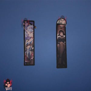 May include: Two rectangular keychains with anime-style illustrations. One features a character in blue and red attire, the other a character in a black dress. Both have a black border and a silver keyring.