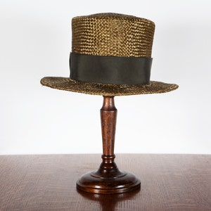 Peut inclure: Un chapeau haut de forme en paille marron avec un ruban vert, présenté sur un support à chapeau en bois.