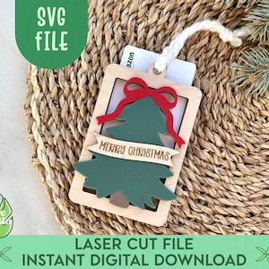 Puede incluir: Una etiqueta de regalo navideña de madera con un árbol verde, un lazo rojo y las palabras "MERRY CHRISTMAS". La etiqueta es rectangular con un marco marrón claro y una cuerda blanca. El texto "LASER CUT FILE INSTANT DIGITAL DOWNLOAD" está en la parte inferior.