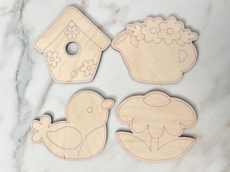 May include: Four unfinished wooden cutouts of spring-themed designs: a birdhouse, a watering can with flowers, a bird, and a flower. The cutouts are ready to be painted.