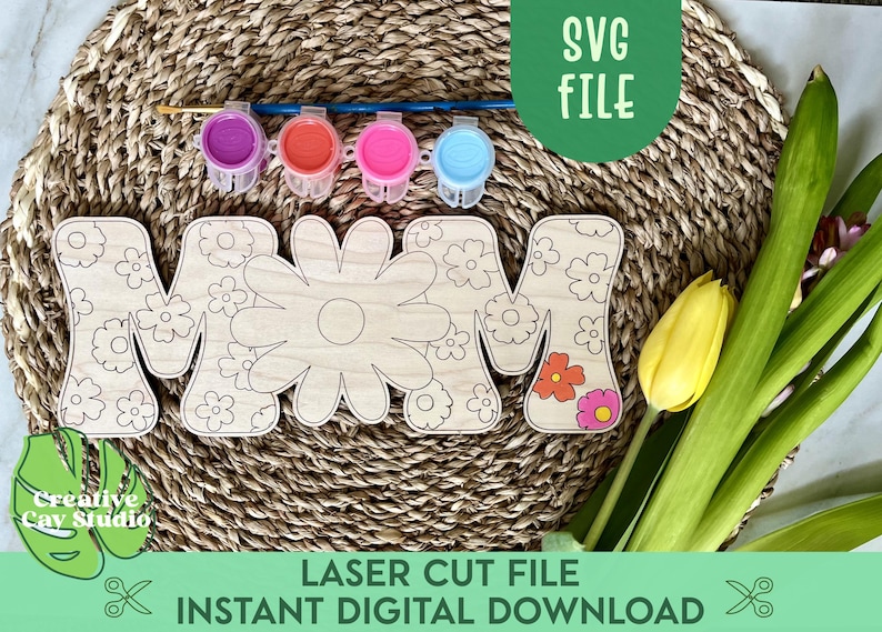 May include: A wooden cutout of the word "MOM" with a floral design. The letters are surrounded by a woven straw mat and there are four small jars of paint in the background. The text "LASER CUT FILE INSTANT DIGITAL DOWNLOAD" is at the bottom of the image.