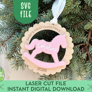 May include: A wooden Christmas ornament with a pink rocking horse design, the name "Coraline", and the year 2025. The ornament is surrounded by a scalloped edge and the text "BABY'S FIRST CHRISTMAS". The ornament hangs from a white ribbon.