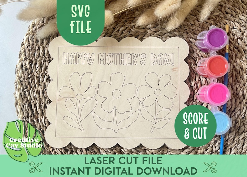 May include: A laser cut wooden sign with a scalloped edge, featuring the text "HAPPY MOTHER'S DAY!" and three stylized flower designs. The sign is ready for painting with included paint pots in pink, red, purple, and blue.