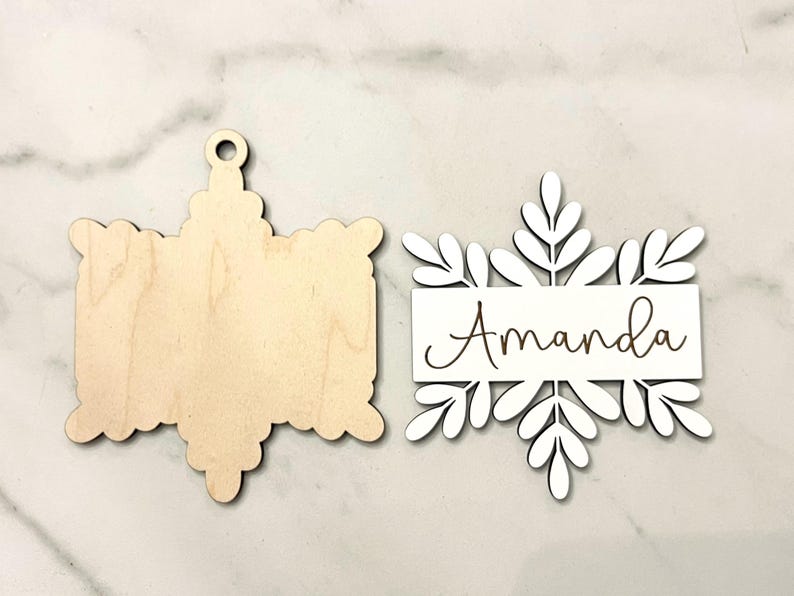 May include: Two unfinished wooden ornaments, one shaped like a snowflake with the name "Amanda" engraved on it, and the other shaped like a star.