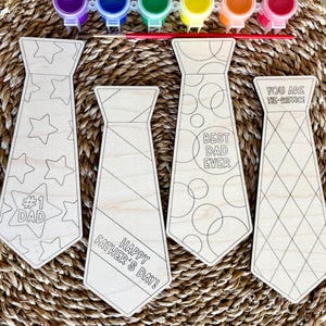 May include: Wooden tie-shaped craft kits with various designs and text, including "#1 Dad", "Happy Father's Day!", "Best Dad Ever", and "You Are Tie-riffic!". Paint pots and a paintbrush are included, perfect for a Father's Day gift.