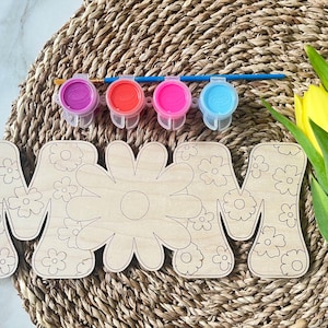 May include: Wooden craft kit featuring the word "MOM" with a floral design. The kit includes four small paint pots in purple, red, pink, and blue.