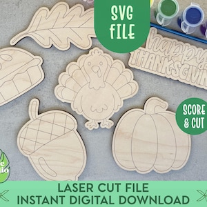 Op de afbeelding: Een verzameling onafgewerkte houten uitsparingen met een kalkoen, een pompoen, een eikel, een blad en een bordje met de tekst Happy Thanksgiving. De set bevat kleine verfpotjes en een blauwe kwast voor diverse knutselprojecten.