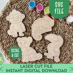 May include: Wooden laser-cut animal shapes, including a monkey, chameleon, leopard, and toucan, are arranged on a woven mat. Paint pots and brushes are visible. The text "SVG FILE", "SCORE & CUT", and "LASER CUT FILE INSTANT DIGITAL DOWNLOAD" are also present.