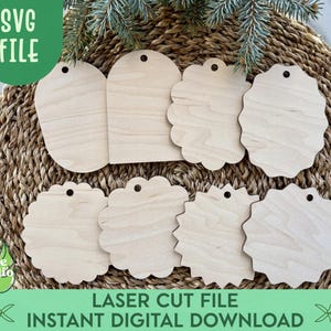 Może przedstawiać: Kolekcja niewykończonych drewnianych etykiet w różnych kształtach, w tym wzory z ząbkami i zaokrąglone, z małymi otworami do zawieszania. Etykiety ułożone są na tkanej powierzchni z wikliny, z gałązkami zieleni. Obraz zawiera tekst "SVG FILE" i "LASER CUT FILE INSTANT DIGITAL DOWNLOAD".