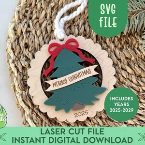 Könnte beinhalten: Weihnachtsschmuck aus Holz mit einem grünen Tannenbaum-Design, einer roten Schleife und den Worten "Merry Christmas" auf einem Banner. Der Schmuck enthält das Jahr 2025 und die Jahre 2025-2029. Der Text "SVG FILE" und "LASER CUT FILE INSTANT DIGITAL DOWNLOAD" sind ebenfalls vorhanden.