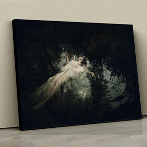 May include: A woman in a white dress lies in a dark, watery setting. The dress is flowing around her, and the water is reflecting the light from above. The scene is mysterious and ethereal.