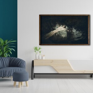 May include: A framed photograph of a woman in a white dress lying in a dark forest setting. The photograph is hanging on a white wall above a light wood and white entertainment center.