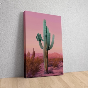 May include: A tall, green cactus stands in a desert landscape with a pink sky. The cactus has multiple arms and is surrounded by smaller cacti and shrubs.