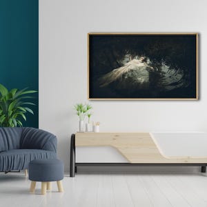 May include: A framed photograph of a woman in a white dress lying in a body of water surrounded by greenery. The photograph is displayed on a white wall above a wooden and white media console.
