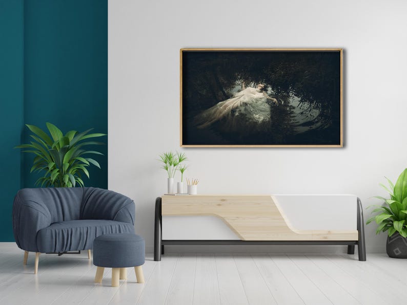 May include: A framed photograph of a woman in a white dress lying in a body of water surrounded by greenery. The photograph is displayed on a white wall above a wooden and white media console.