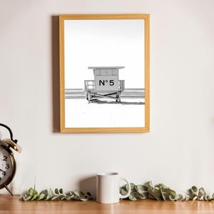 May include: A black and white photograph of a lifeguard stand on a beach. The stand is numbered "N&deg; 5" and is framed in a light wood frame.