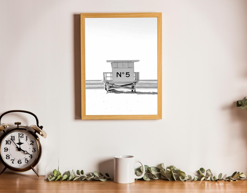May include: A black and white photograph of a lifeguard stand on a beach. The stand is numbered "N&deg; 5" and is framed in a light wood frame.