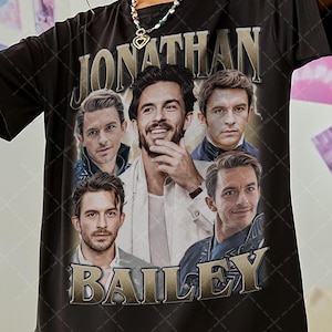 May include: Black t-shirt featuring the name "JONATHAN BAILEY" in gold lettering, with a collage of five portraits of Jonathan Bailey. The shirt has a diamond pattern background.
