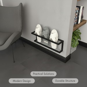 Op de afbeelding: Een zwarte metalen schoenenrek aan een grijze muur, met drie paar slippers. Twee paar zijn wit en één is grijs. De rek heeft een rechthoekig, minimalistisch ontwerp. De woorden "Practical Solutions", "Modern Design" en "Durable Structure" worden weergegeven.
