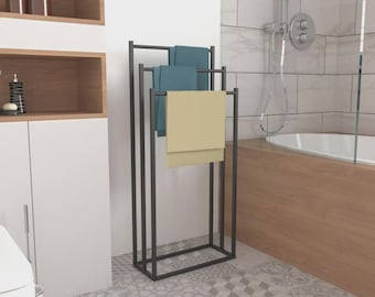 May include: A black metal towel rack with three bars, holding two teal and one beige towel. The rack is rectangular and stands in a bathroom with patterned tile flooring and a white bathtub.