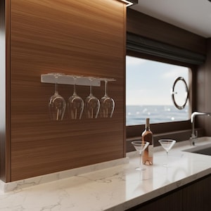 Può includere: Una moderna cucina con un mobile in legno e un piano di lavoro bianco. Quattro bicchieri da vino trasparenti sono appesi a un supporto argentato. Una bottiglia di vino e due bicchieri da martini sono sul bancone, con vista sul mare dalla finestra.
